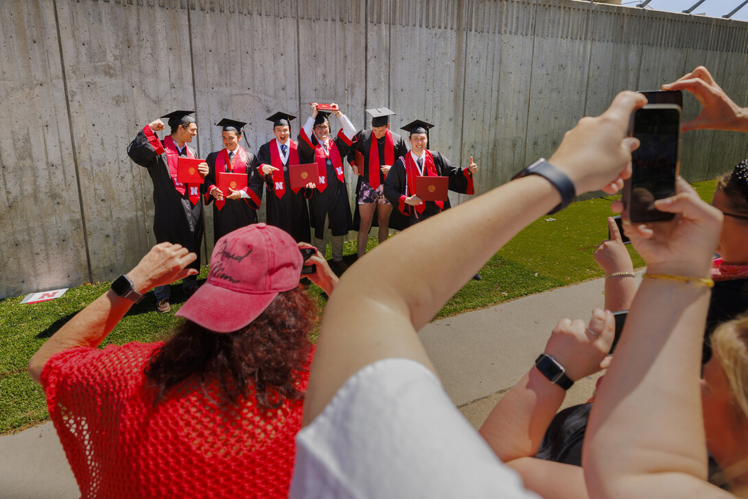 Six male graduates pose for photographs outside of Memorial Stadium.