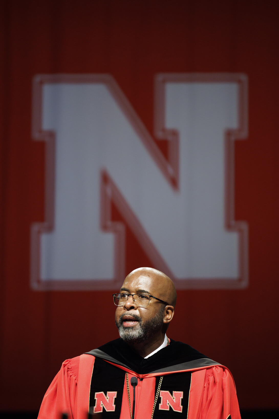 Chancellor Rodney D. Bennett speaks at a lecturn with a white Nebraska block N behind him.