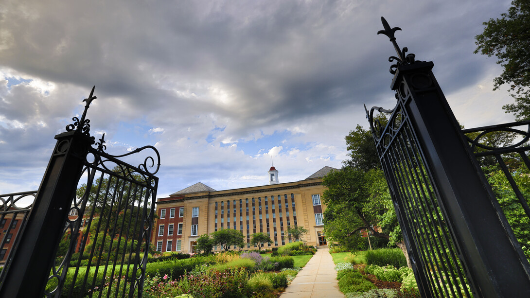 Black metal garden gates frame Love Library South on a cloudy day.