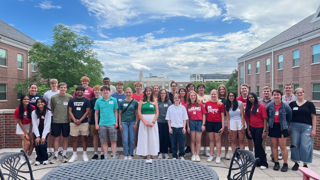 Thirty-one Husker students, all members of the Jeffrey S. Raikes School of Computer Science and Management, pose on the rooftop of the Kauffman Academic Residential Center on a partly cloudy day. The Nebraska Union and Nebraska State Capitol are visible in the background.