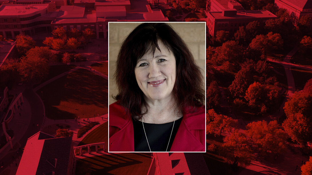 Color portrait of Carolyn Ducey, Ardis B. James Curator of Collections for the International Quilt Museum, on a red campus background.