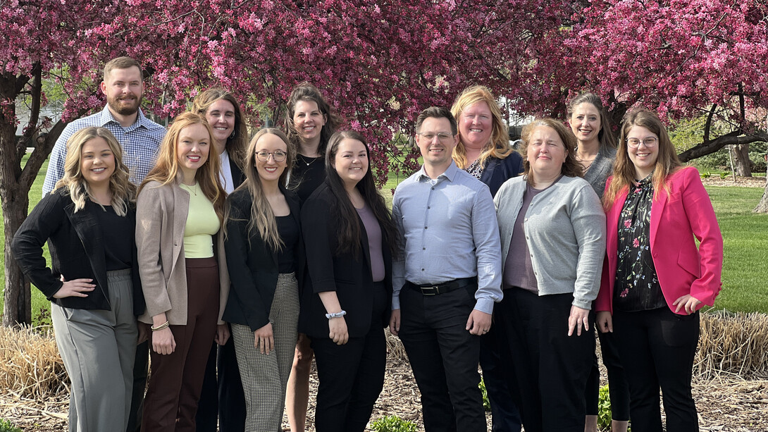 Ten women and two men — all rural Nebraska attorneys who recently completed the College of Law's Children's Justice Attorney Education Fellowship program — pose near blossoming trees in springtime.