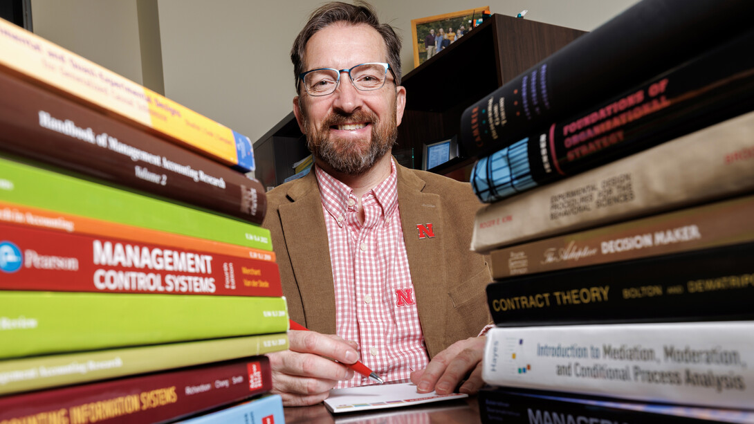 Todd Thornock poses with a pen and pad of paper, between two stacks of business textbooks.