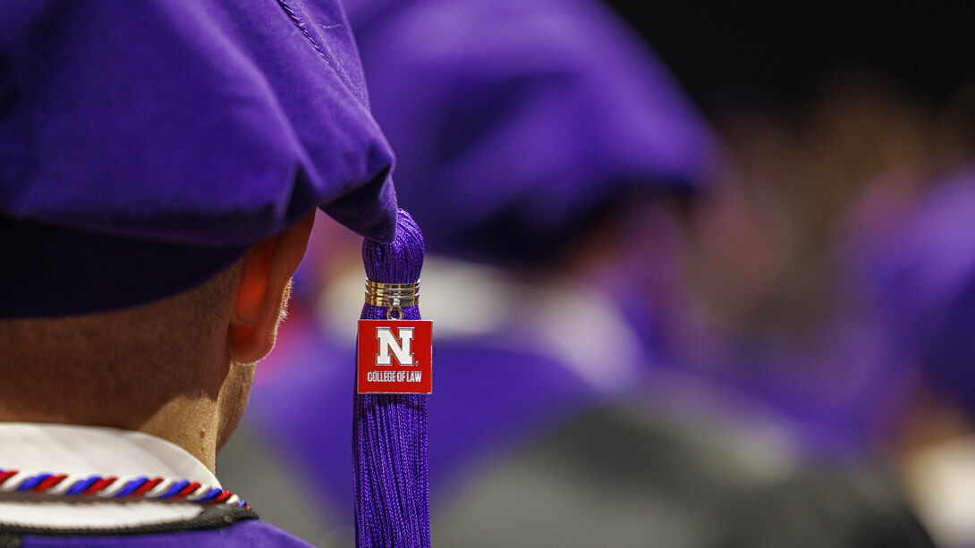 A close-up of a University of Nebraska College of Law graduate from behind. He is wearing a purple tam with a purple tassel. From the tassel hangs a red, square pendant with the Nebraska block N and the words "College of Law."