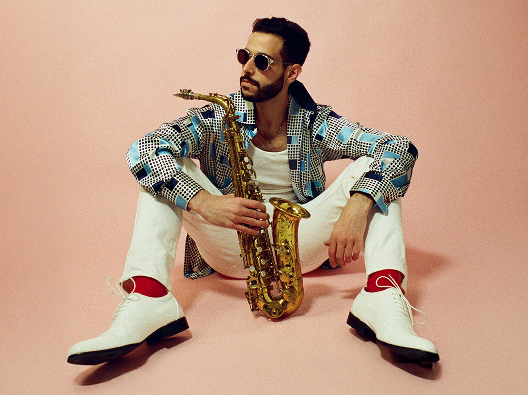Color portrait of Sam Greenfield, seated on the ground with a saxophone.