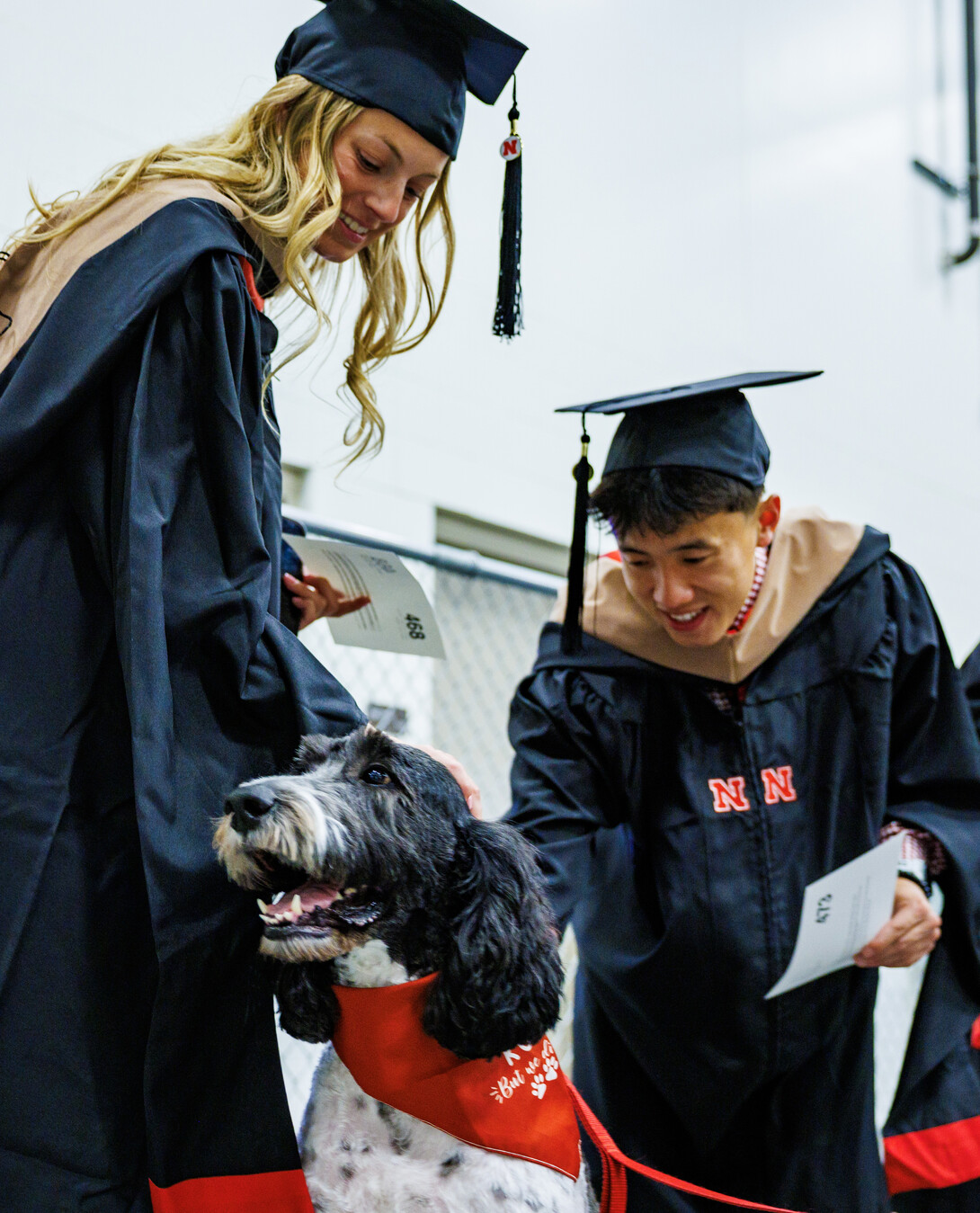 Mallory Schuh and Alvan Tran pet Cash the therapy dog before the graduate and professional degree ceremony May 16 at Pinnacle Bank Arena.