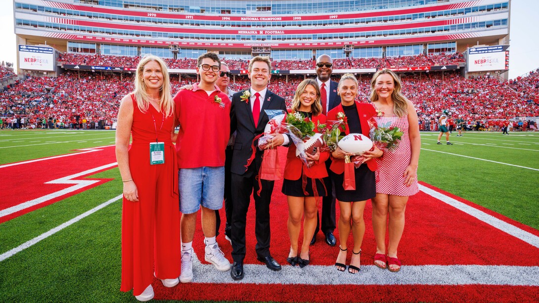 Four women and three men in red and black stand pose for a photograph at midfield in Memorial Stadium.