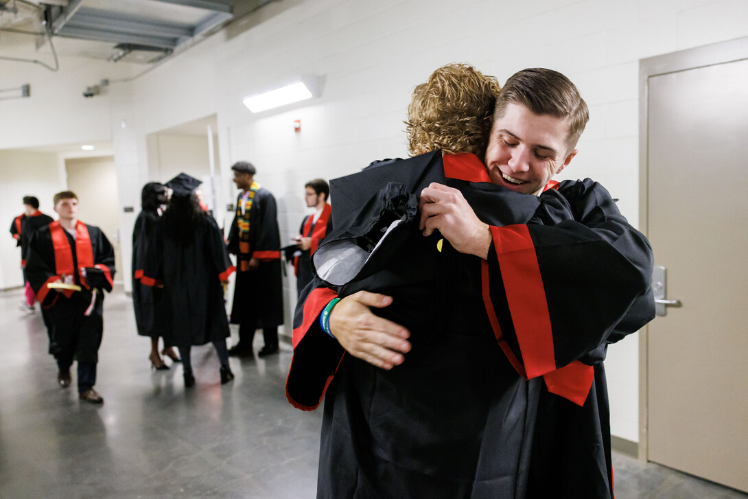 Two male graduates embrace in a hallway of Pinnacle Bank Arena. Other graduates can be seen in the background.