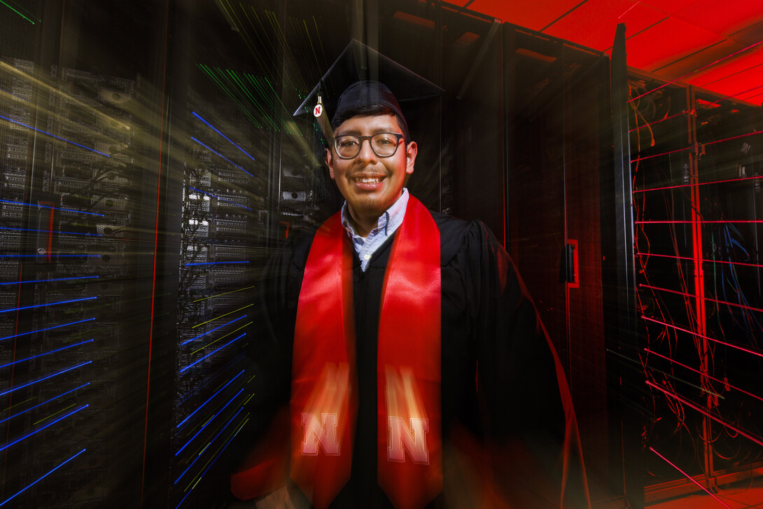 Bryan Chavez stands in front of a super computer. 