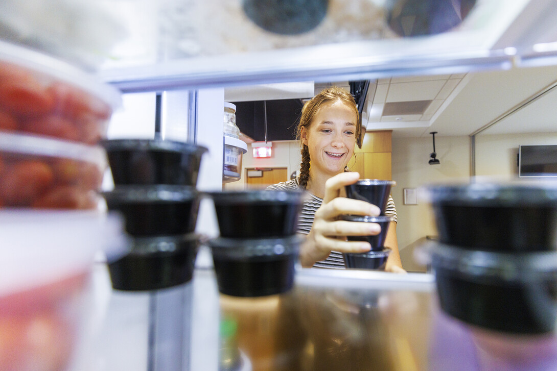 Brenna Mazour, a senior in psychology and dietetics, rearranges containers of shredded cheese in the wellness kitchen refrigerator. The refrigerated items will be added to the kits when the meals are picked up.