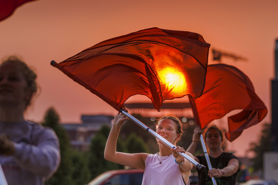 The rising sun appears to burn a hole through the flag of Cornhusker Marching Band color guard member Jaedynn Shively, a sophomore from Lincoln.