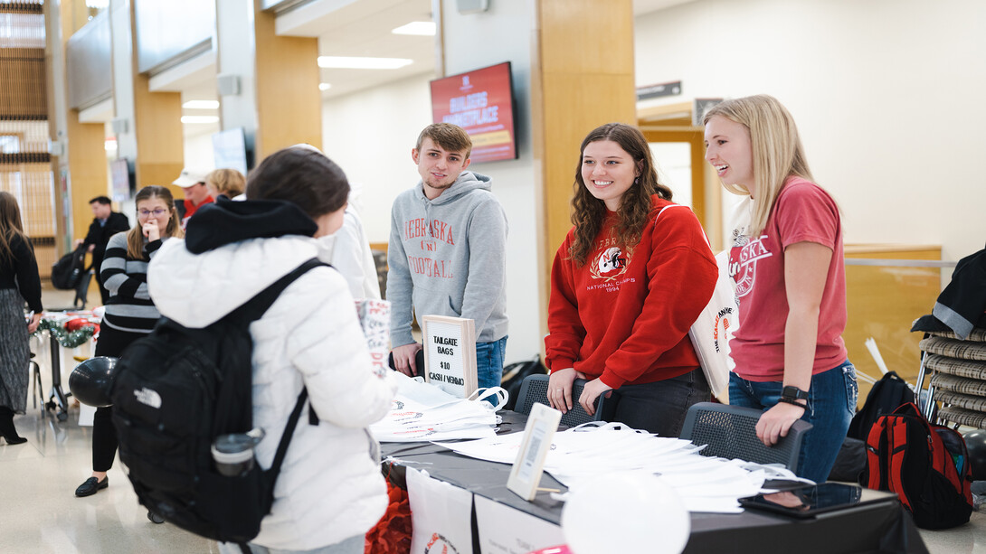 Jordan Westbroek stands in the very right of the photo in a red Nebraska t-shirt, talking to another student in a white coat and backpack about Clifton Strengths.