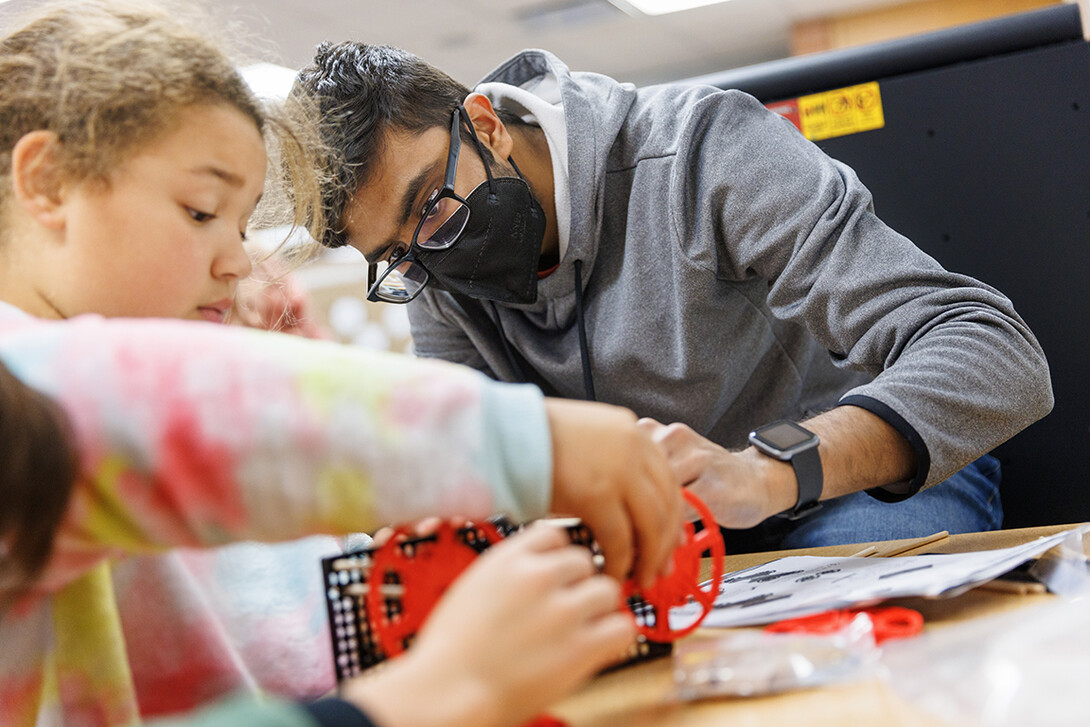 Rohan Tatineni helps a student build her rubber-band powered car.