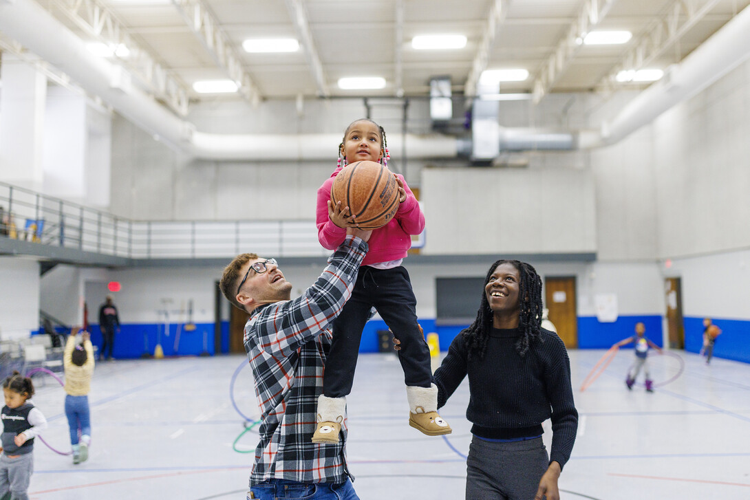 Ben Bentzinger, a senior in criminal justice, and Francisca Lawson Tettevie a graduate student with CYAF, help Journey shoot a basket at the Malone Center.