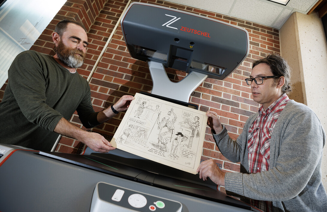 Richard Graham, Associate Professor of University Libraries, right, and John Wiese place an Oz Black cartoon onto the scanner bed to digitize the drawing. Graham and Wiese are building an online archive of editorial cartoons from Nebraska alumnus Oz Black. These cartoons are mostly from the 1920s and 1930s, and ran in Nebraska newspapers headquartered in Lincoln.