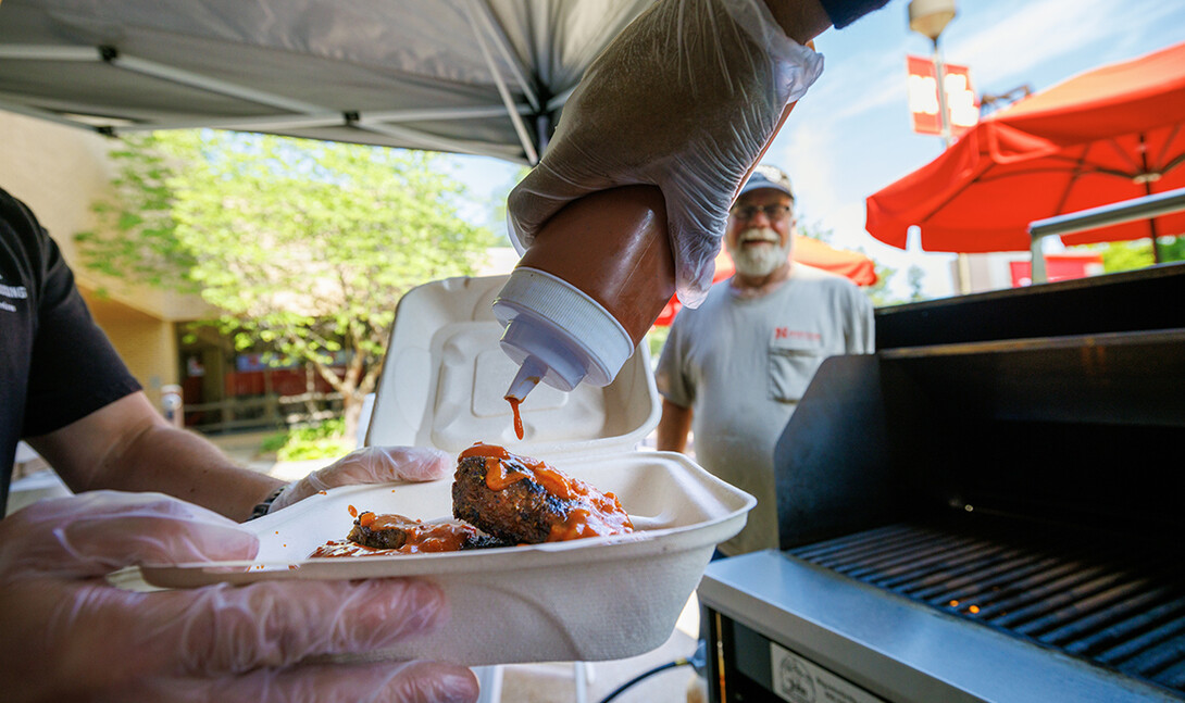 A cook adds Oklahoma BBQ sauce to an order of ribs at an East Campus grill out.