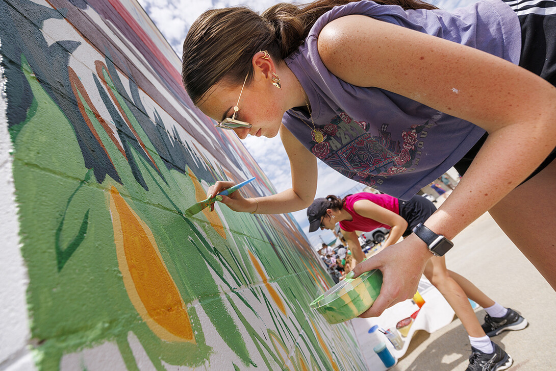 Lea Bushey, a senior in graphic design, paints stems of grass on the mural. ARTS 398 - Special Topics in Studio Art III taught by Sandra Williams. The class painted a mural at the Premier Buick, Chevrolet, and GMC dealership in Beatrice.