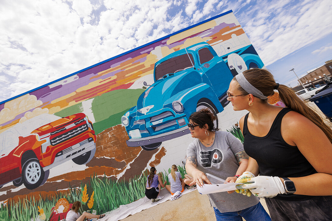 Sandra Williams, center, and Maddie Vanderbur, a senior in graphic design and the mural’s designer, look over a printout of the mural.