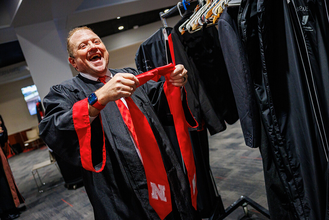 Corrie Svehla puts on his graduation sash backstage before commencement exercises.