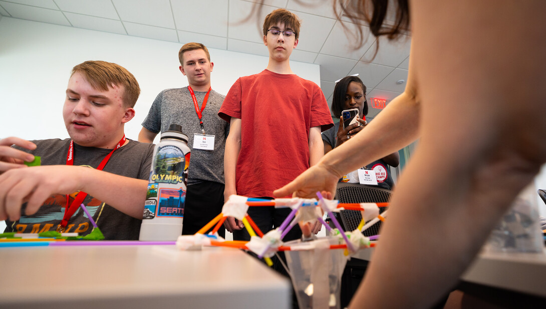 oe Lake (red shirt) and Ryne Callahan watch as Rachel Rose, coordinator of engineering outreach, places heavy metal washers into a cup to see how much weight their straw-and-tape bridge can hold. The two, both high school juniors, participated in the engineering camp offered as one of Nebraska 4-H's Big Red Summer Academic Camps.