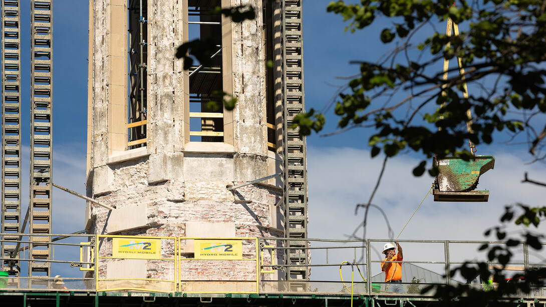 Steve Raumaker grabs a guide rope to pull a hopper to the platform where he and other Kehm Contractors employees are steadily removing exterior stone from Mueller Tower. The stone is lifted off the tower in the hopper and placed onto waiting flatbed trucks to be cleaned and repaired before returning to the tower later in the summer.