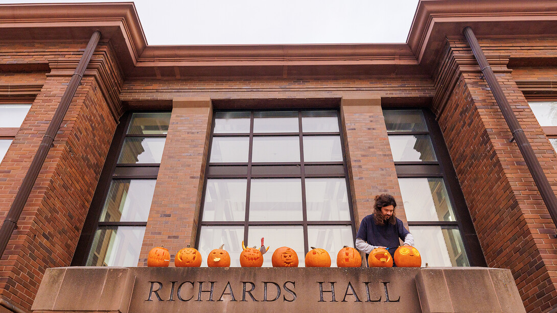 Joseph Holmes, Art Fabrication Space Manager in the School of Art, Art History & Design, sets finished pumpkins on the top of the north entrance to Richards Hall during the Sculpture Club’s pumpkin carving meeting. Oct. 29, 2025