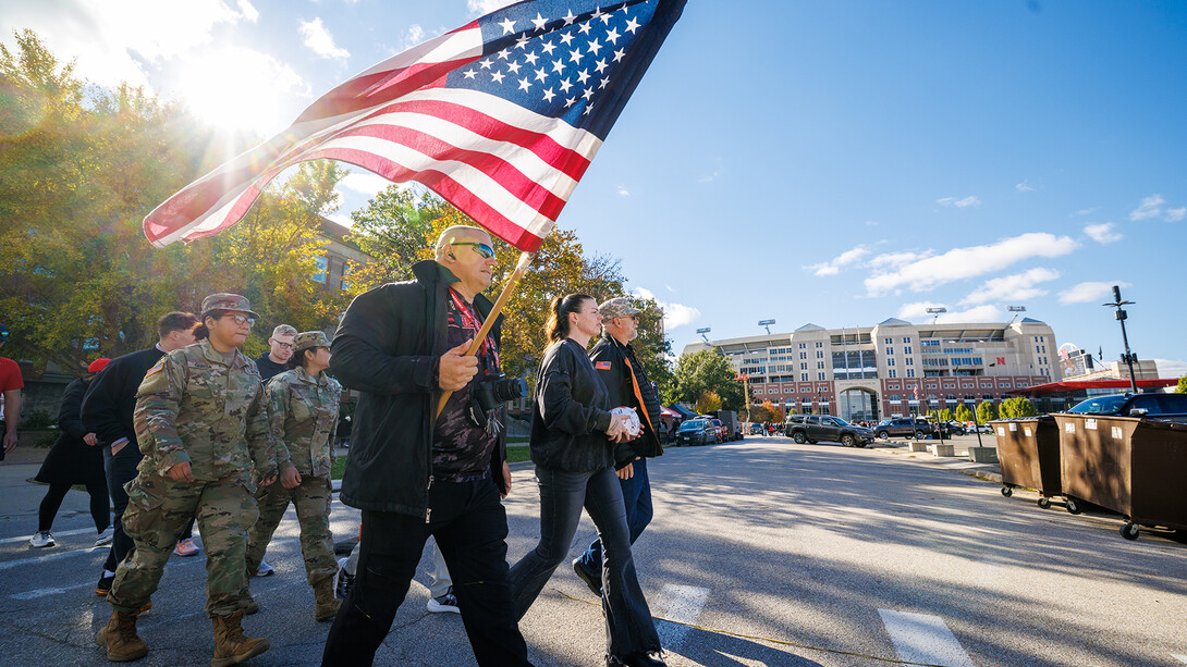 A group of ROTC students and veterans march the game ball to Memorial Stadium on city campus for gameday. Emily Dietzman holds the ball in the middle.
