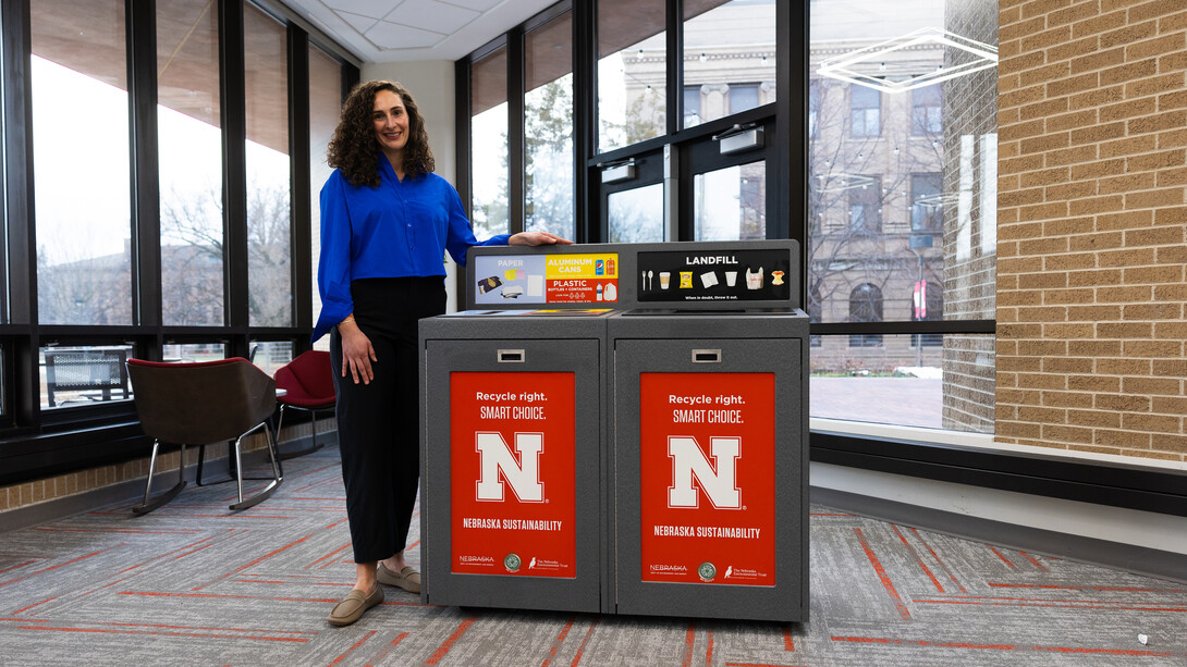 A woman stands next to a recycling station.
