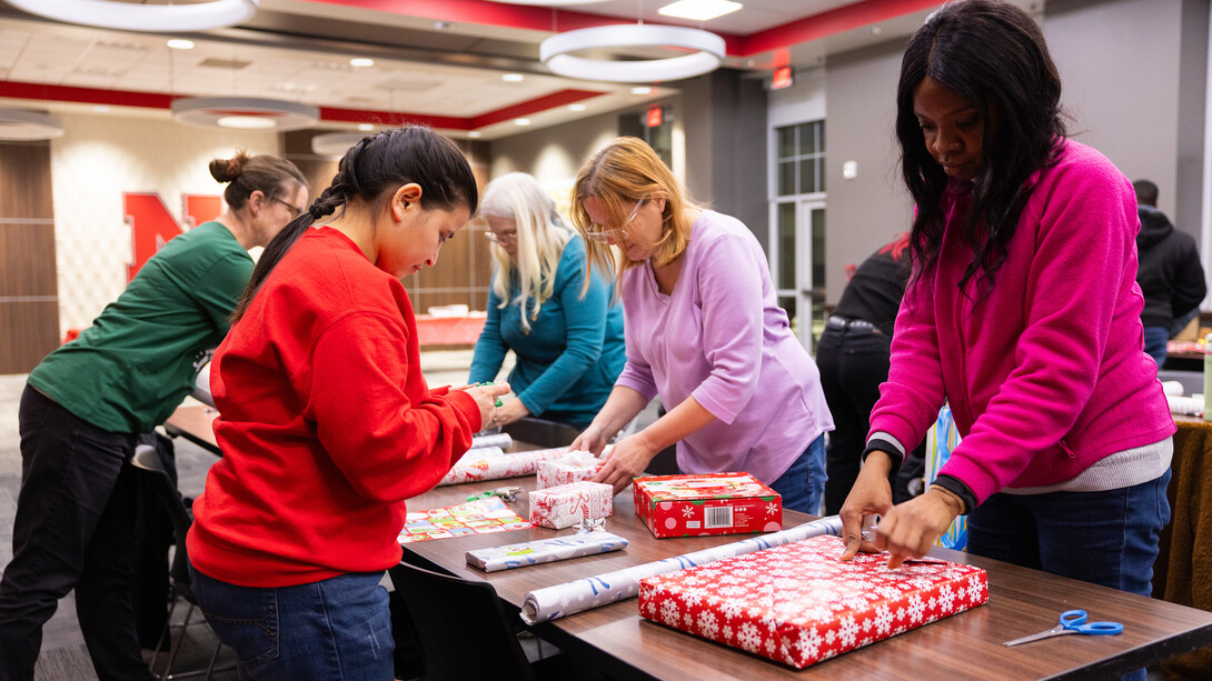 People stand around a table wrapping gifts.