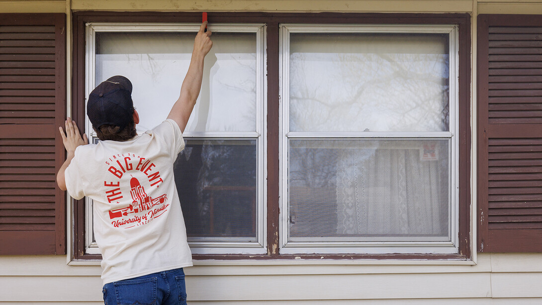 A student prepares a window frame for painting at a home during a campus volunteer day.
