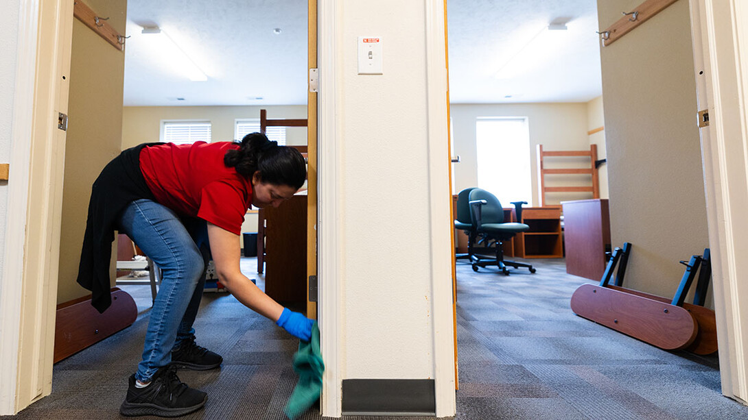 A woman cleans the door to a dorm room.