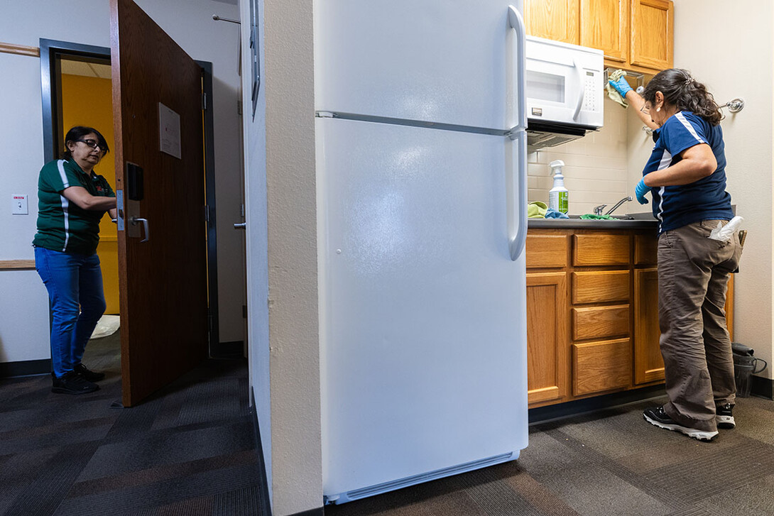 Two people clean in a dorm kitchenette.