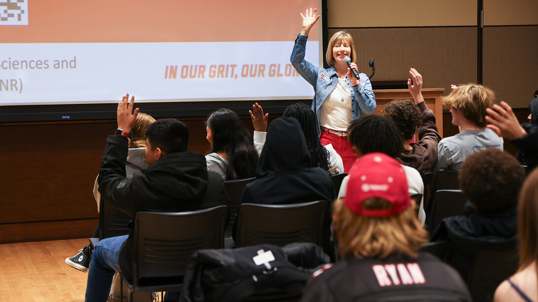 Sue Ellen Pegg, with short blond hair wearing a jean jacket over a white top, welcomes various Omaha Public Schools students sitting before her.
