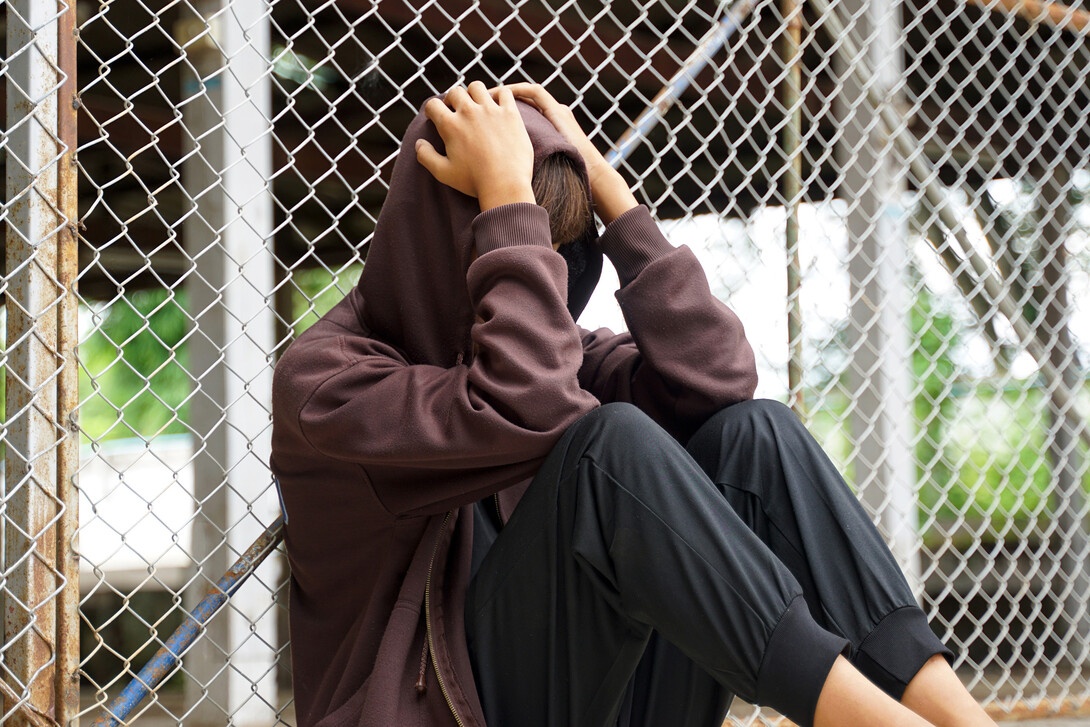 A teen sits against a fence.