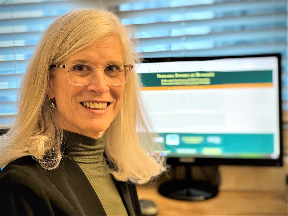 Beth Dotan is shown with a screen capture of the “Nebraska Stories of Humanity: Holocaust Survivors and WWII Veterans" project behind her.