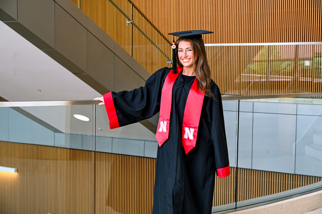 Lena Lankas stands in her cap and gown in the College of Business stairway.