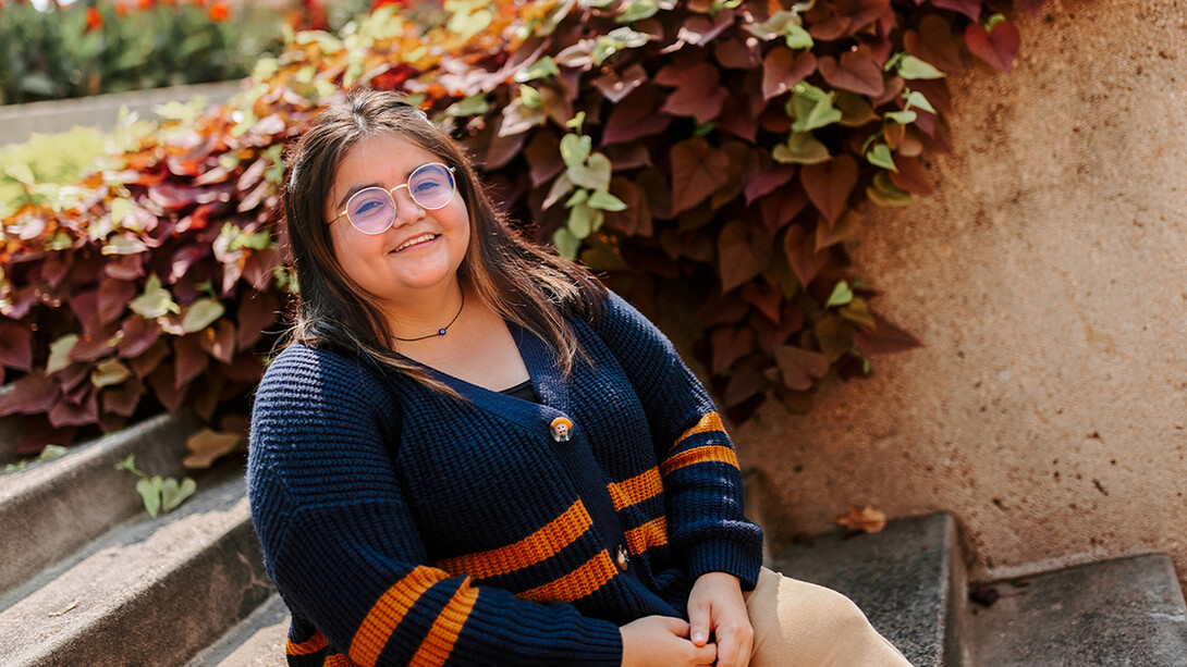 Dulce Isabel Garcia sits in front of a wall of greenery on campus.