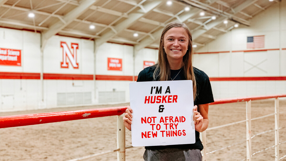 Olson smiles for a photo in the Equestrian Team's practice facility on East Campus. She holds a sign that reads "I'm a Husker and not afraid to try new things".
