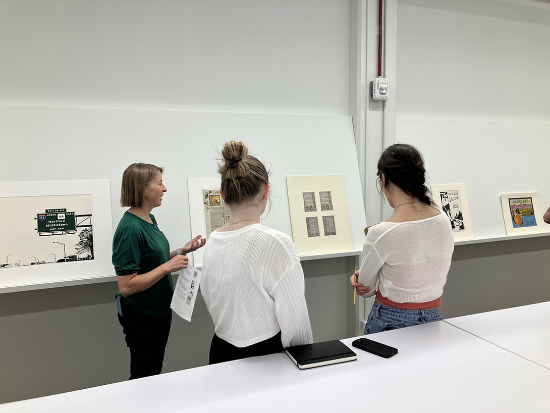 Three people stand in front of a selection of works of art featuring typography.