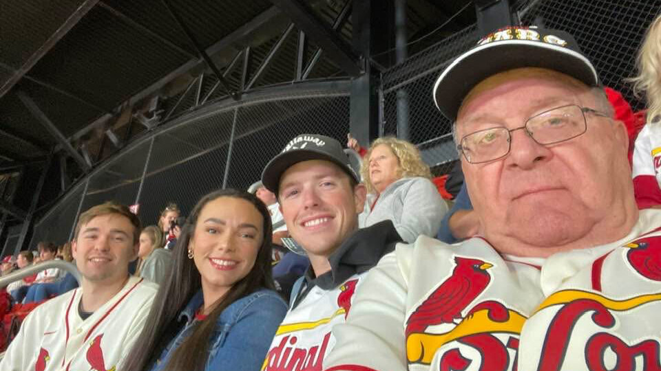 Image of Tom Simons sitting with friends in Busch Stadium watching a St. Louis Cardinals baseball game.