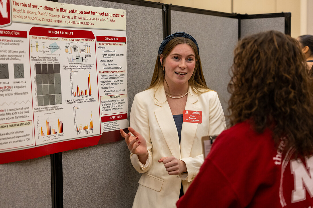 Undergraduate Brigid Toomey discusses her presentation, "The role of serum albumin in filamentation and farnesol sequestration," to a poster judge at the 2023 symposium.