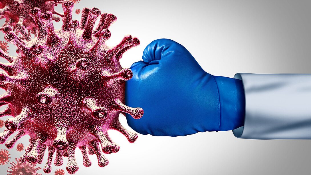 Doctor wearing a blue boxing glove punching a COVID-19 model.