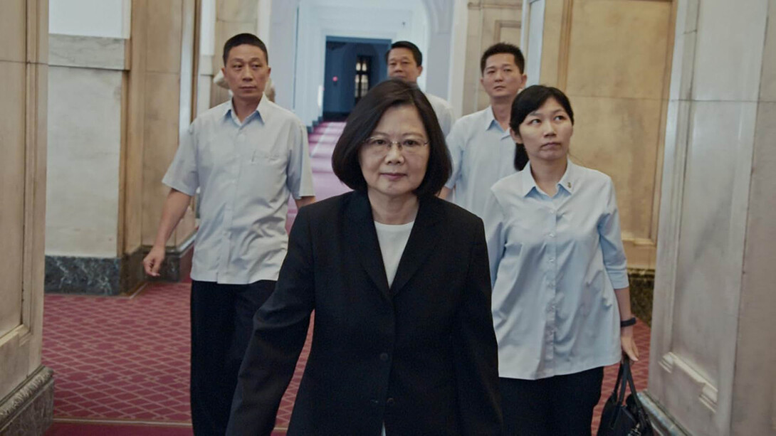 The President of Taiwan walks down the center of a hall accompanied by four people behind her. 